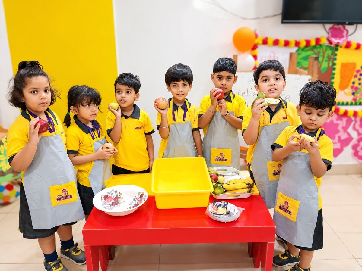 Kidzee Ramnagar children in aprons holding fresh fruit during a healthy-eating activity